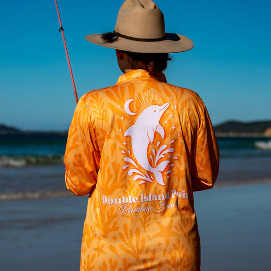 Person wearing an orange shirt with a dolphin design on a beach