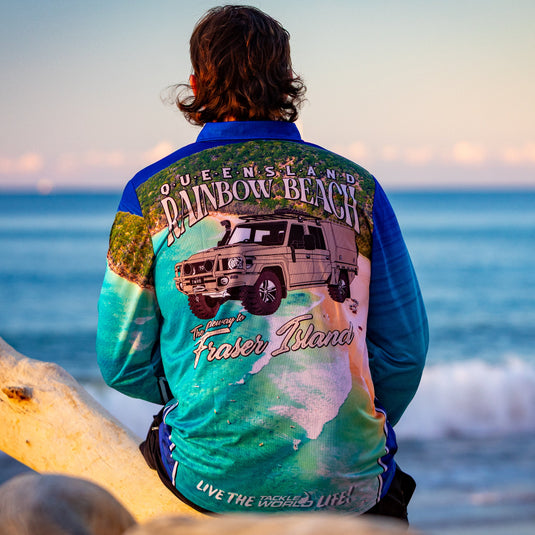Person wearing a colorful shirt with a graphic design sitting on a beach.
