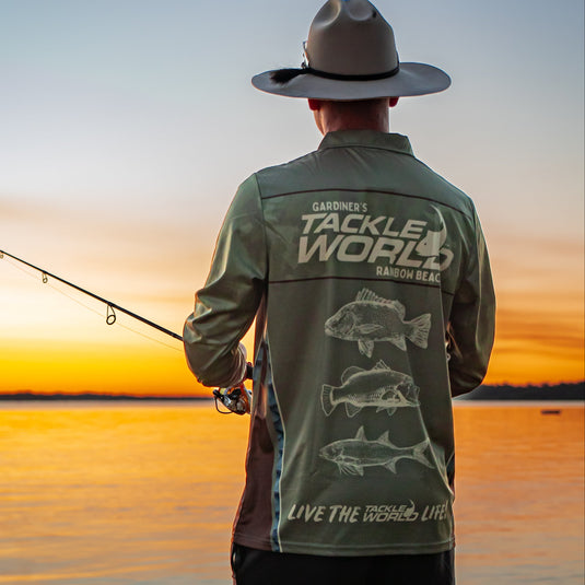 Man wearing a 'Gardiner's Tackle World' shirt by a lake at sunset
